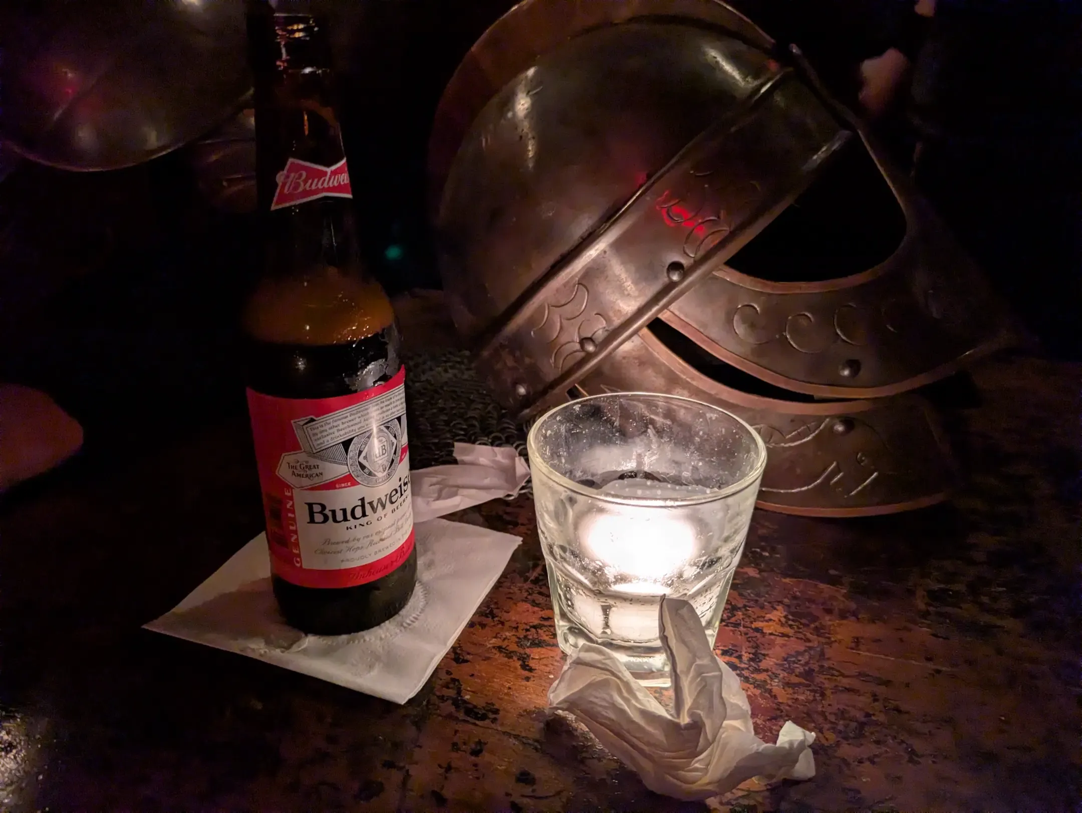 Title: Gladiator, Description: A beer and a metal helmet lit by a candle on a bar table