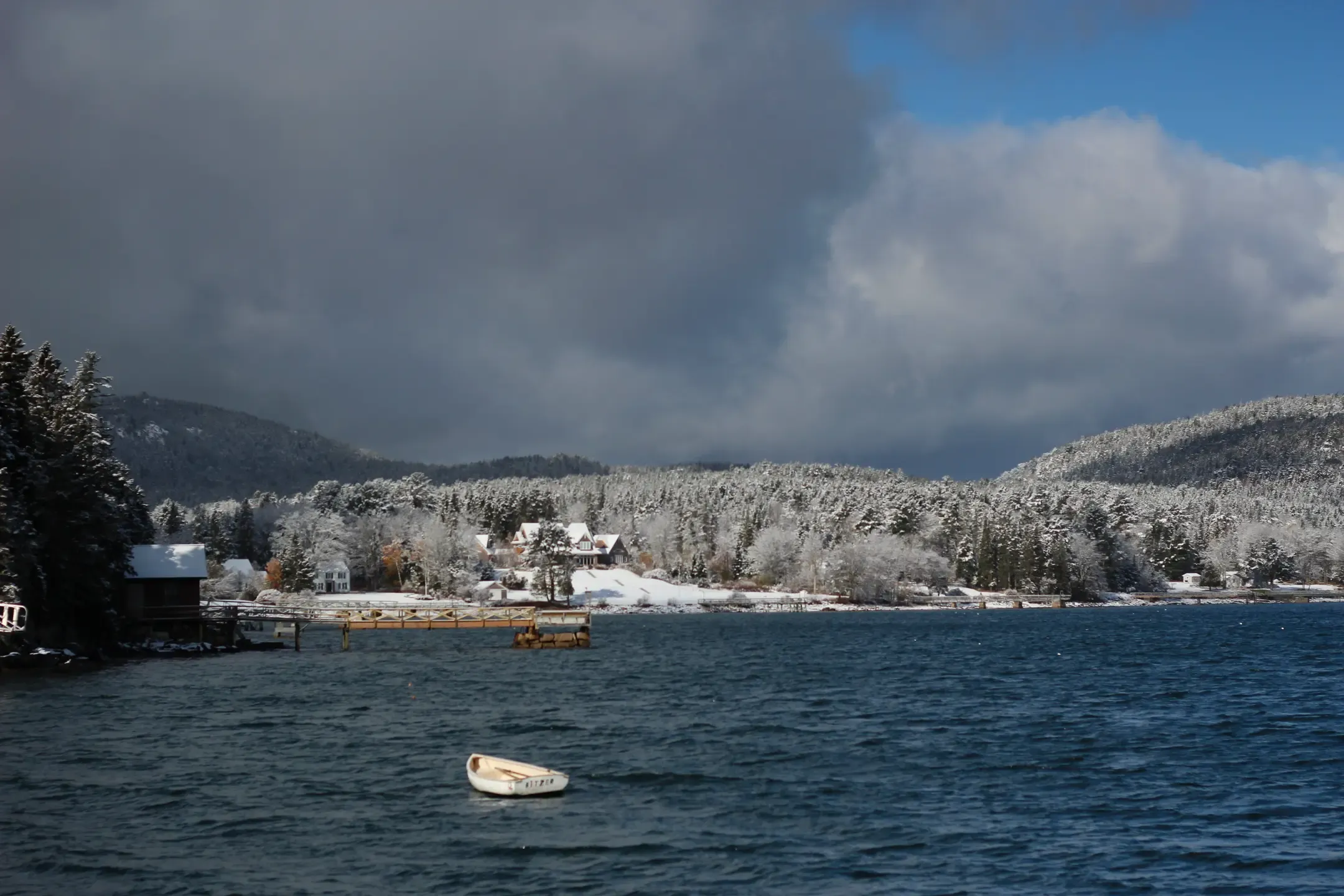 Title: Winterboat, Description: A row boat in a cove during winter, with snowy mountains and storm clouds in the background